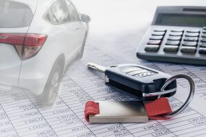 Tisch, Autoschlüssel liegen neben Taschenrechner auf ausgedruckten Zahlentabellen